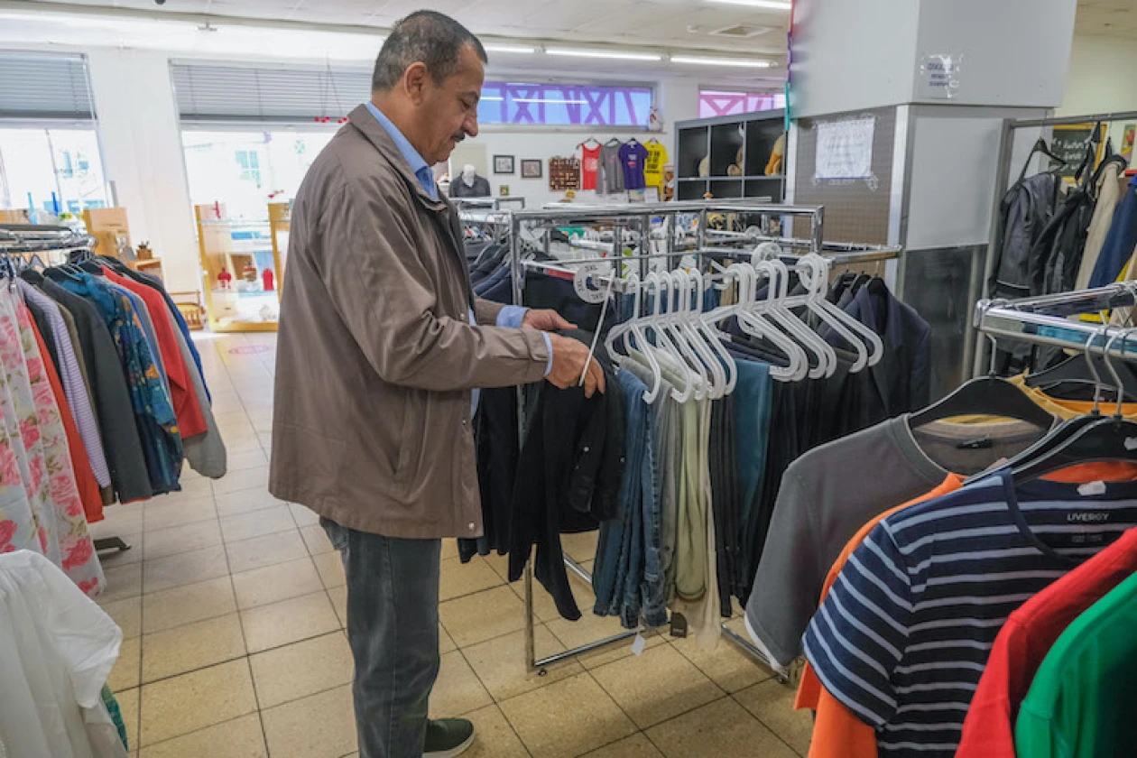 Ein Mann in grauer Jacke schaut auf einem Kleiderst&auml;nder eine dunkle Hose an. Im Hintergrund sind weitere Kleiderst&auml;nder mit verschiedenen Kleidungsst&uuml;cken zu sehen.