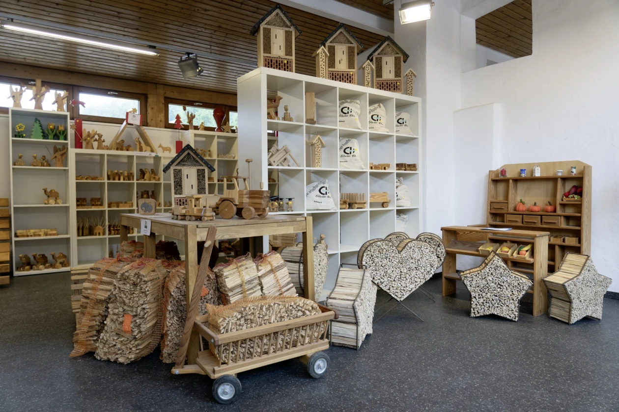 Verkaufsraum mit Holzwaren im Regal. Dekoration und Handwerkskunst, im Vordergrund steht ein beladener Holz-Bollerwagen, im Hintergrund ein Holz-Kauflanden f&uuml;r Kinder.