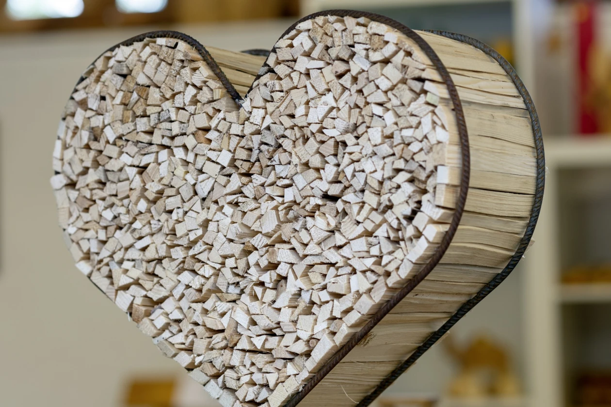 Zu sehen ist ein herzf&ouml;rmiges Metallgestell mit Anz&uuml;ndholz. Im Hintergrund sind Fenster und weitere Holzst&uuml;cke zu sehen.