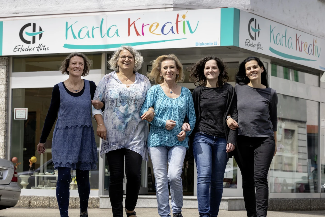 F&uuml;nf Frauen laufen l&auml;chelnd vor einem Gesch&auml;ft namens "Karla Kreativ" mit einer wei&szlig;en und t&uuml;rkisfarbenen Fassade.