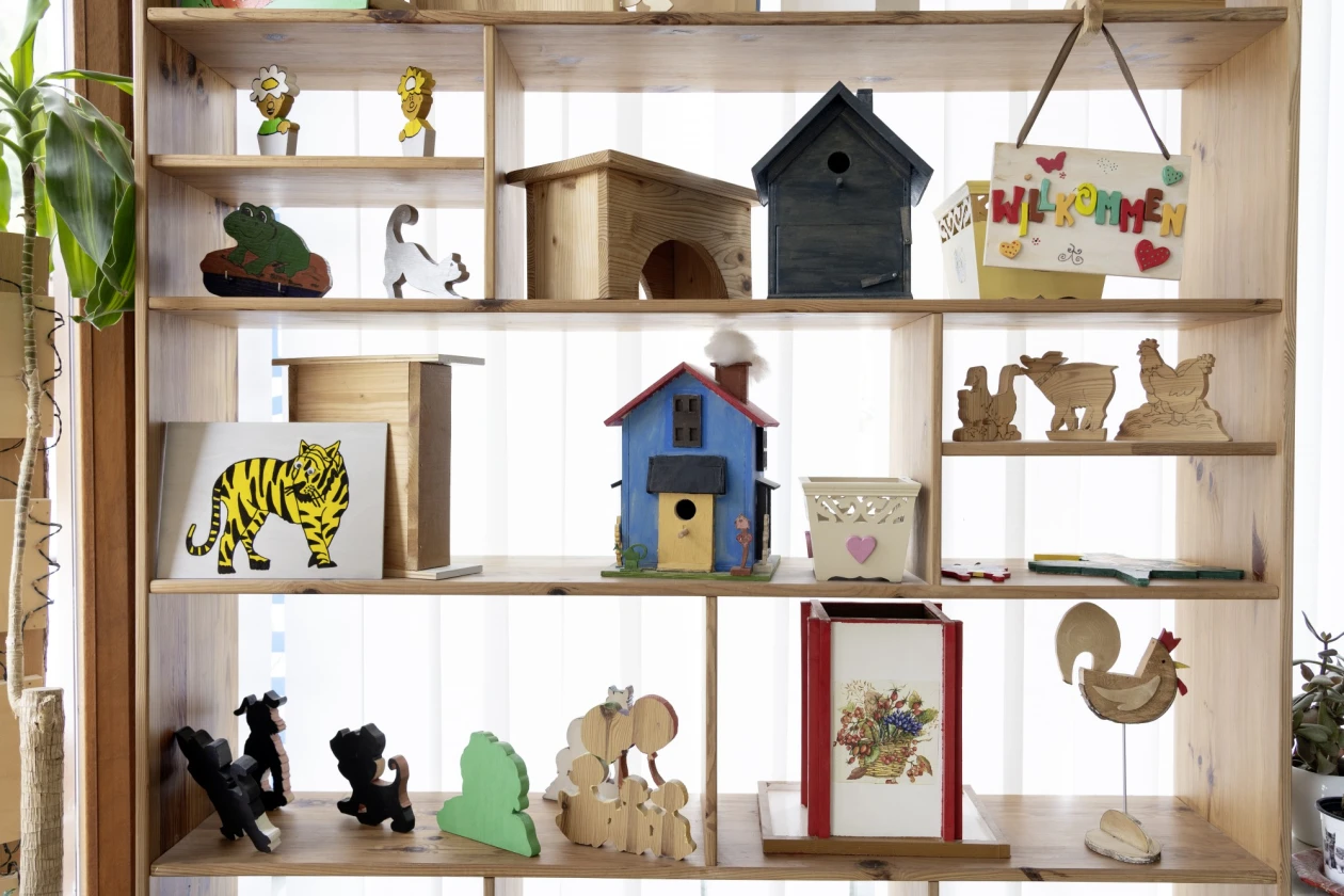 Holzregal mit verschiedenen dekorativen Elementen wie Vogelhaus, Holzfiguren, Silhouetten von Tieren und einem Bild eines Tigers. Die Regale sind in unterschiedlichen Gr&ouml;&szlig;en und Ebenen angeordnet.