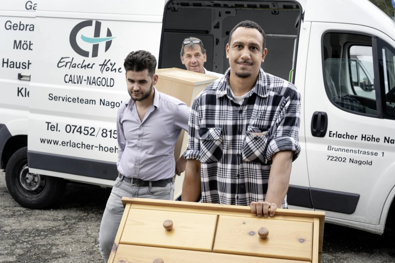 Drei Mitarbeiter des Serviceteams Nagold stehen vor einem Firmenfahrzeug. Der Mann vorn hat seine Hand auf einem Schrank, w&auml;hrend die beiden hinter ihm gemeinsam ein M&ouml;belst&uuml;ck tragen.
