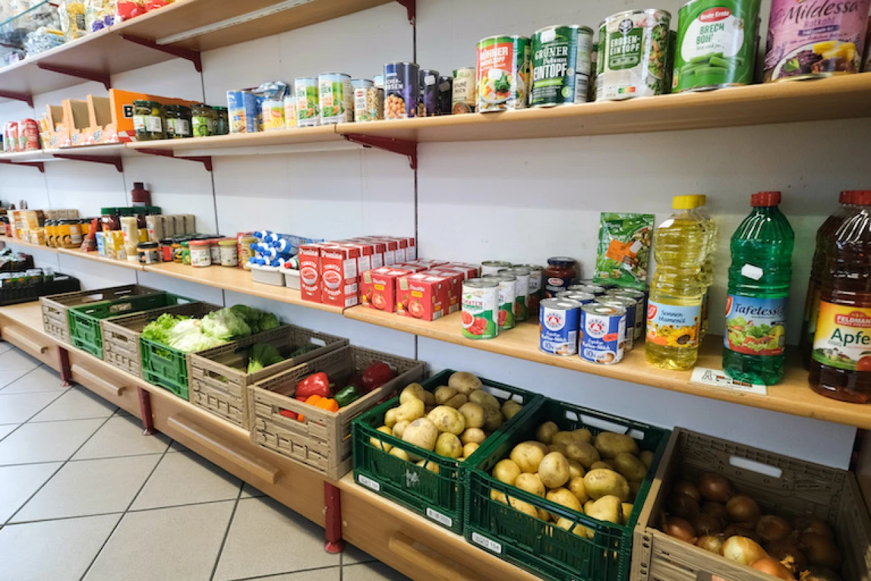 Regal mit verschiedenen Lebensmitteln, Konserven und frischem Gem&uuml;se in Kisten. Die Regale sind ordentlich best&uuml;ckt Kartoffeln, Zwiebeln, Salat und anderen Gem&uuml;sesorten.