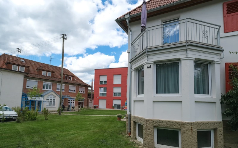 Blick auf ein Geb&auml;udearrangement unterschiedlicher Epochen. Im Vordergrund Teil einer Villa mit turmf&ouml;rmigem Balkon, dahinter ein quaderf&ouml;rmiger, roter Hauskomplex und daneben ein gr&ouml;&szlig;eres Geb&auml;ude aus Klinkerstein mit drei Gauben auf dem Dach.